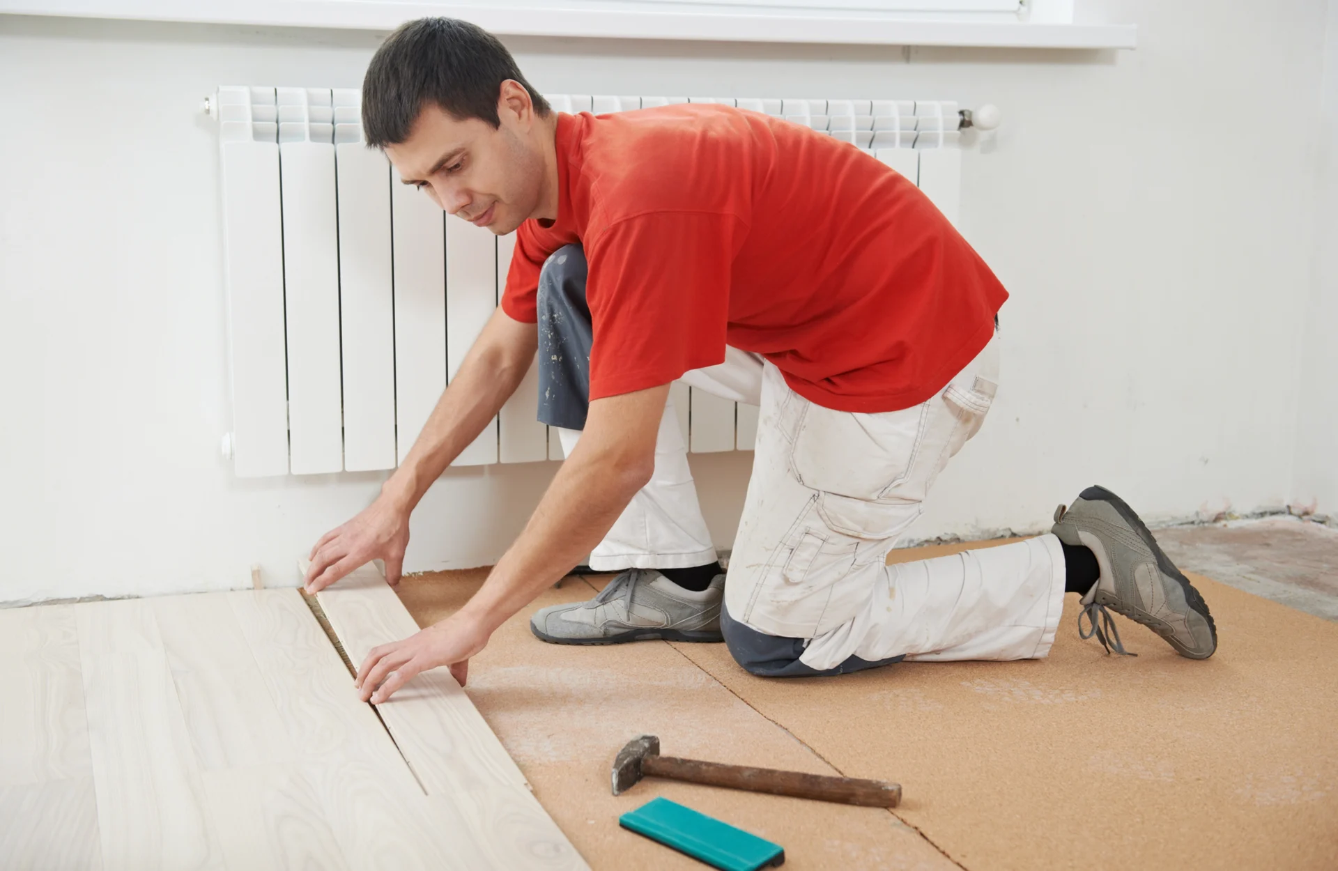Man installing laminate flooring with tools.